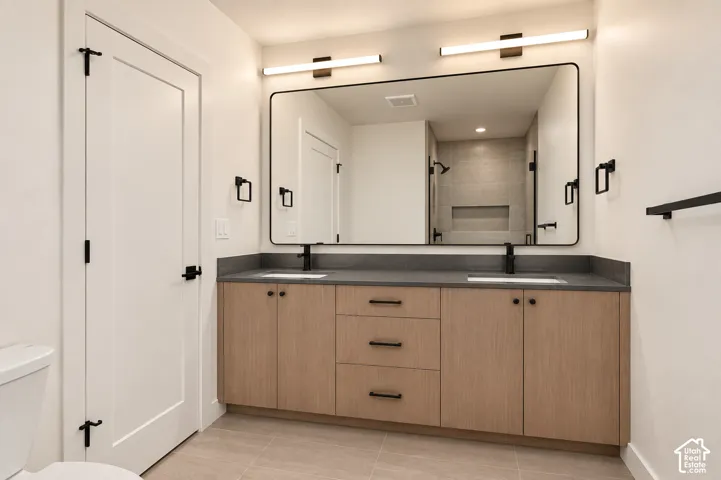 Dual vanity with wood-finish cabinetry, dark countertops, and matte black fixtures