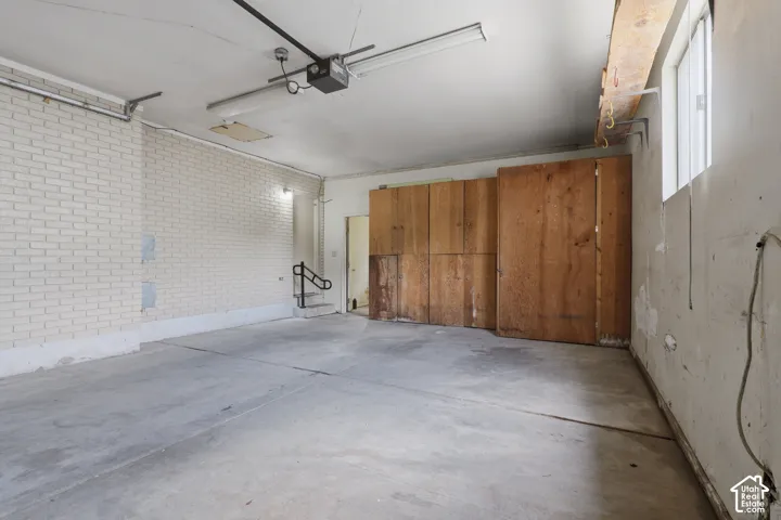 Concrete flooring, white painted brick wall, wood paneling, fluorescent overhead lighting, and an overhead garage door opener mechanism