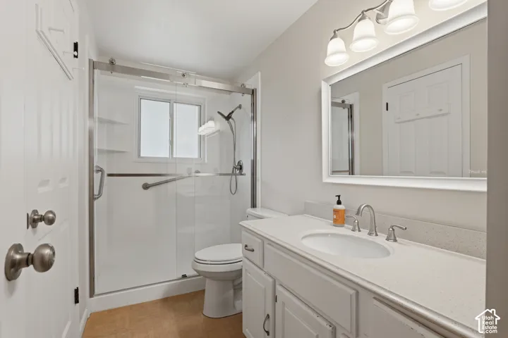 Walk-in shower with sliding glass door, white vanity with integrated sink, dual-handle faucet, wall-mounted mirror, and overhead vanity lighting
