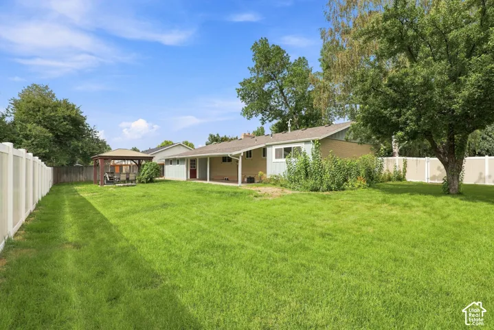 Large expansive grassy yard with a privacy fence, mature trees, and a covered patio area