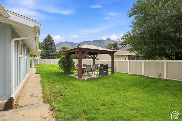 Expansive backyard featuring a gazebo with string lighting, a paver patio, a partial privacy fence, and a mountain backdrop