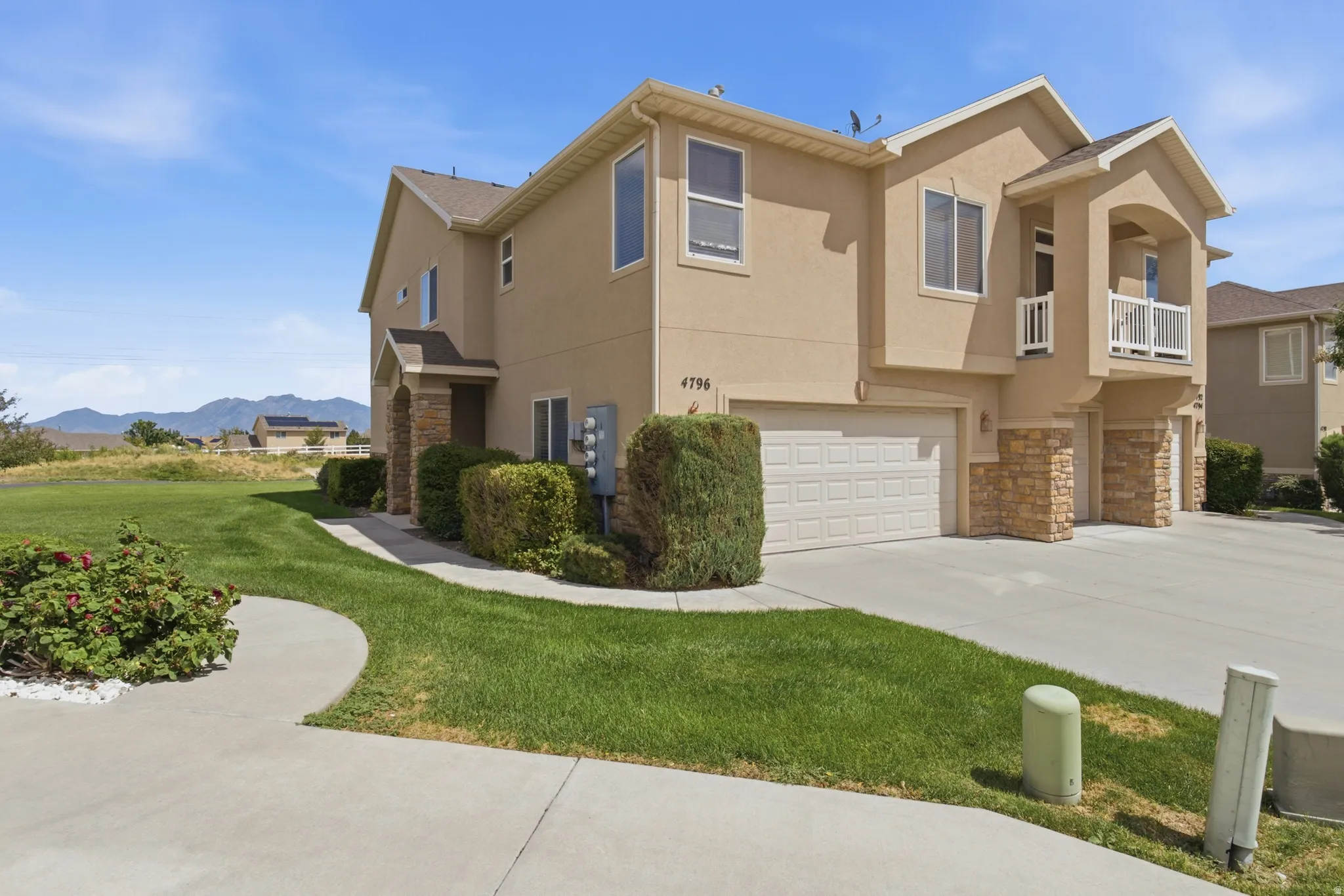Stucco exterior with stone accents, attached two-car garage, concrete driveway, and a second-level balcony with white railings
