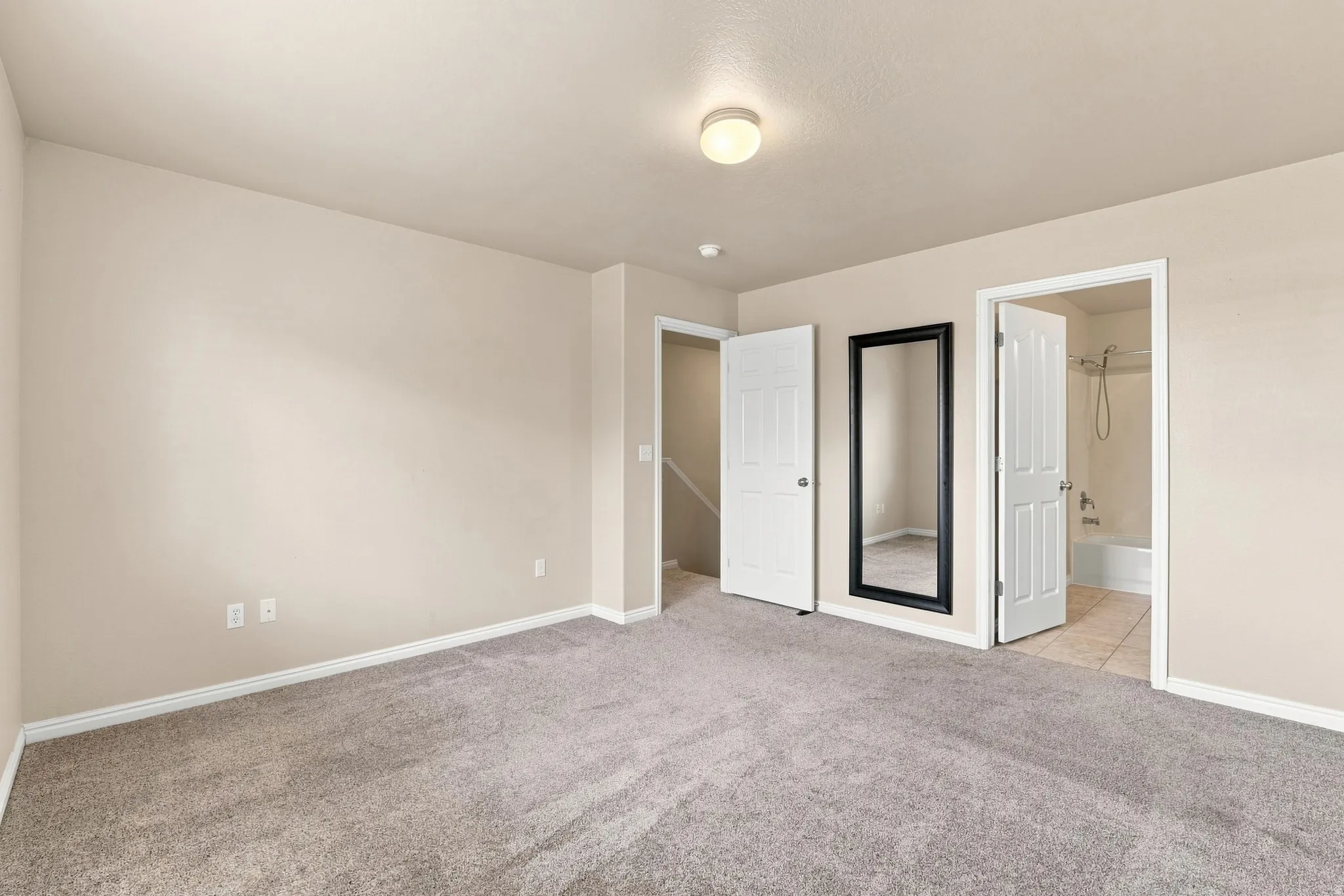 Neutral tone wall paint, flush mount ceiling light fixture, carpet flooring, interior door with paneling, bathroom with tile flooring and tub-shower combination