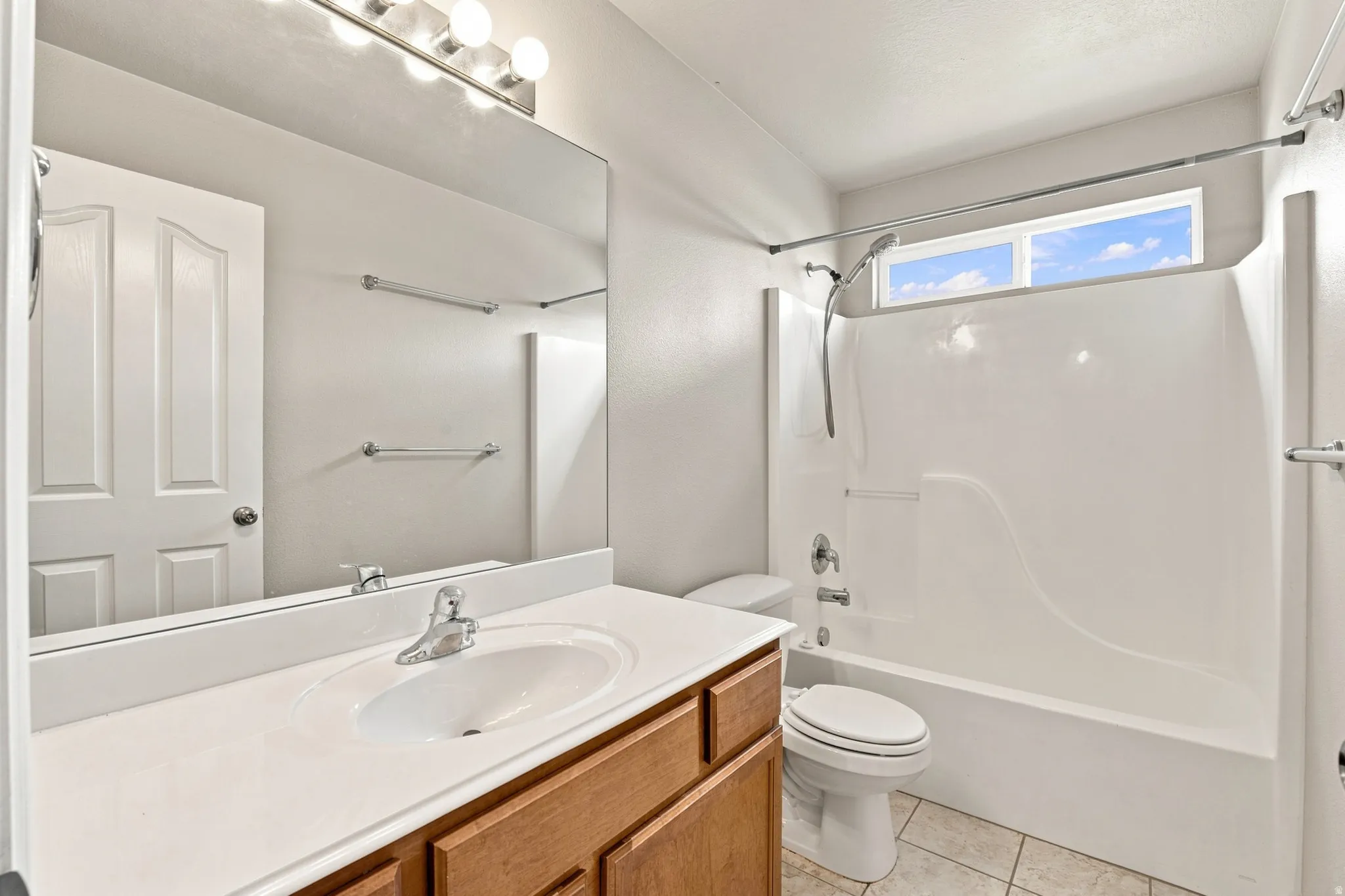 Vanity with integrated sink and chrome faucet, large mirror, full shower and tub combination, privacy window, and tile flooring
