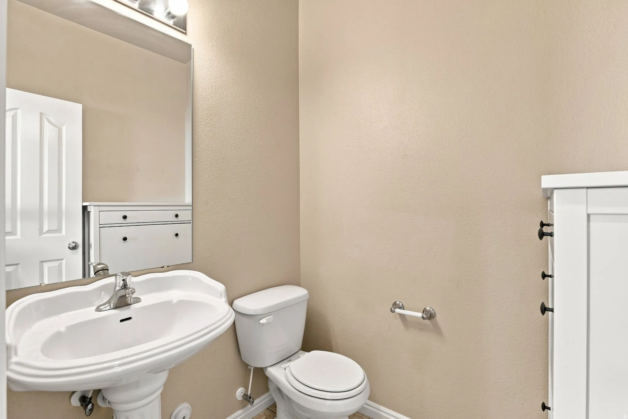 Pedestal sink with chrome faucet, wall-mounted mirror, white commode, and built-in white cabinetry with dark hardware