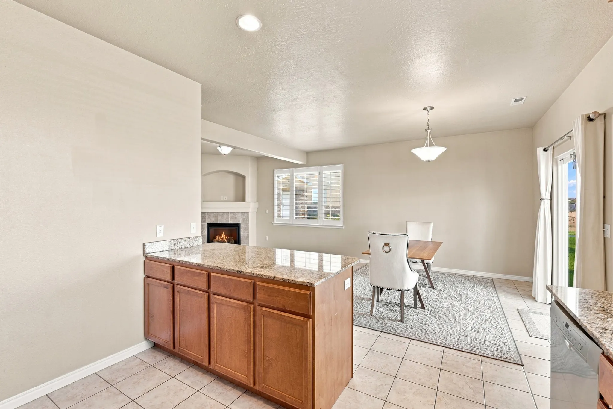 Kitchen island with granite countertop and wood cabinetry, tile flooring, fireplace with mantel, pendant lighting, and a glass-paned exterior door