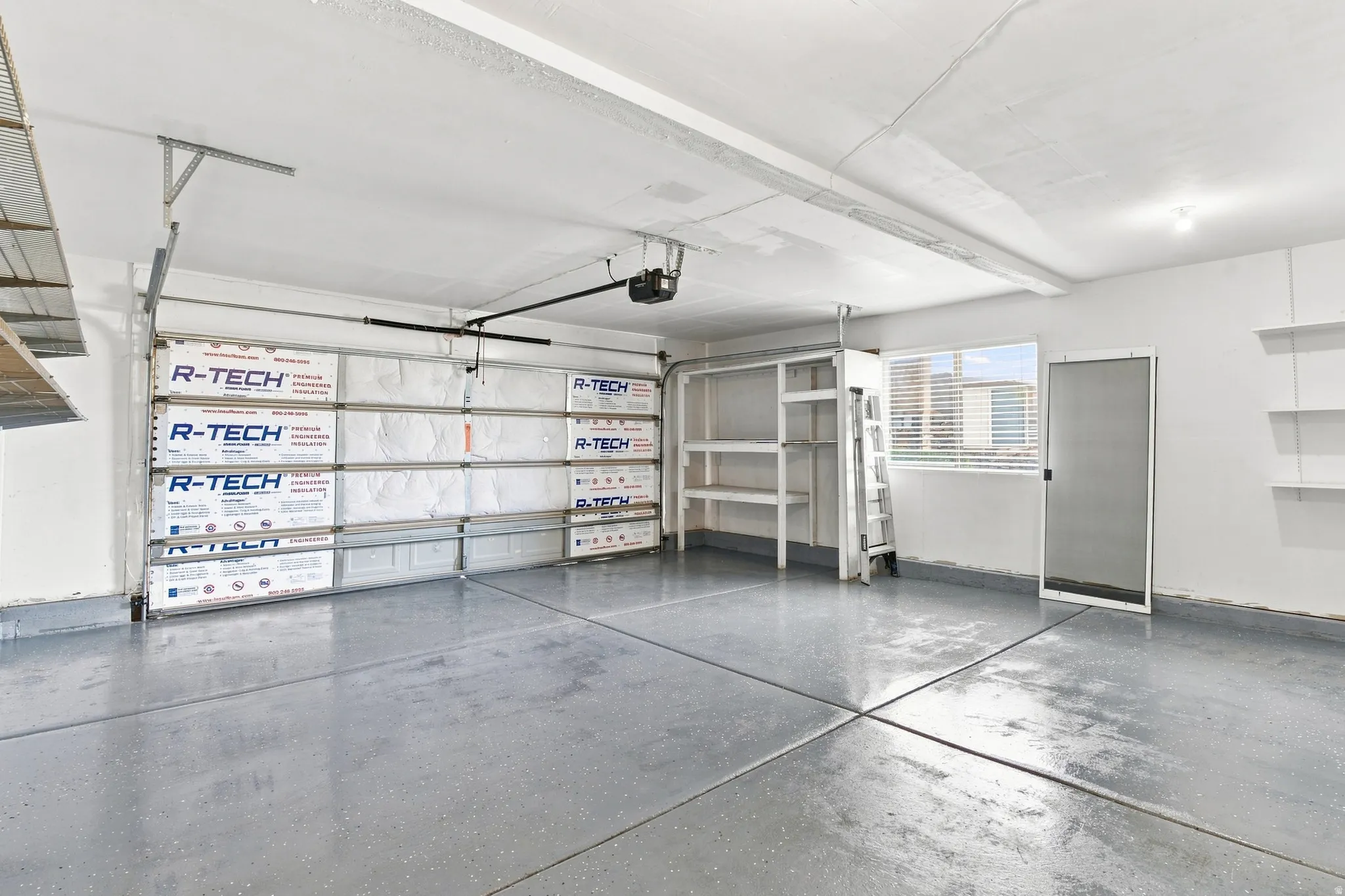 Epoxy-coated concrete flooring, insulated garage door, built-in shelving, mounted wall shelving, and a window for natural light