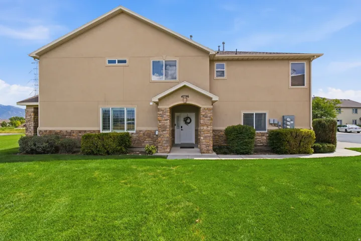 Stucco exterior with a stone veneer accent, covered entry, and established landscaping