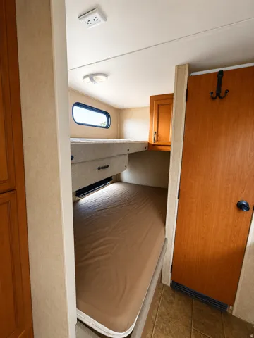 Built-in bunk beds in travel trailerwith integrated lighting, wood-finish cabinetry, and a privacy door