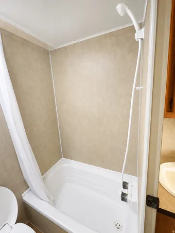 White bathtub with an integrated shower in travel trailer , light-toned wall paneling, and a handheld shower fixture