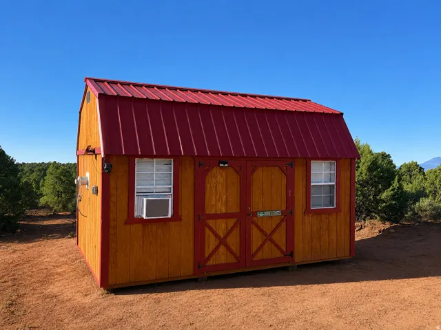 Gambrel roof structure featuring wood siding, red trim, two windows, and double entry doors