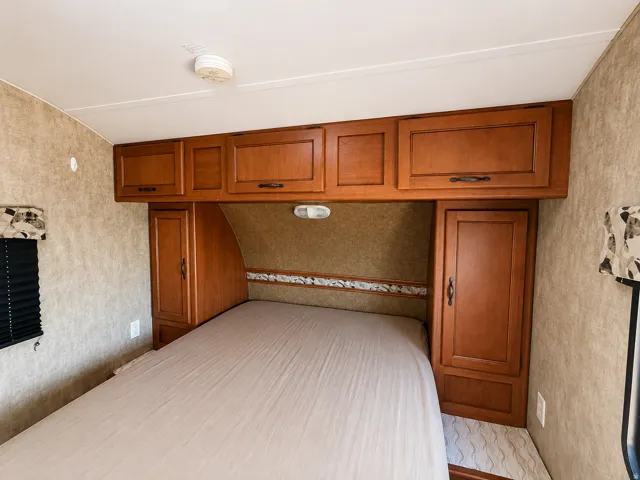 queeen bed in travel trailer Built-in cabinetry with wood-finish doors, overhead storage, and integrated lighting