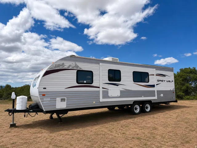 Travel trailer with a grey and white exterior, mountain graphic accents, multiple windows, and dual axles