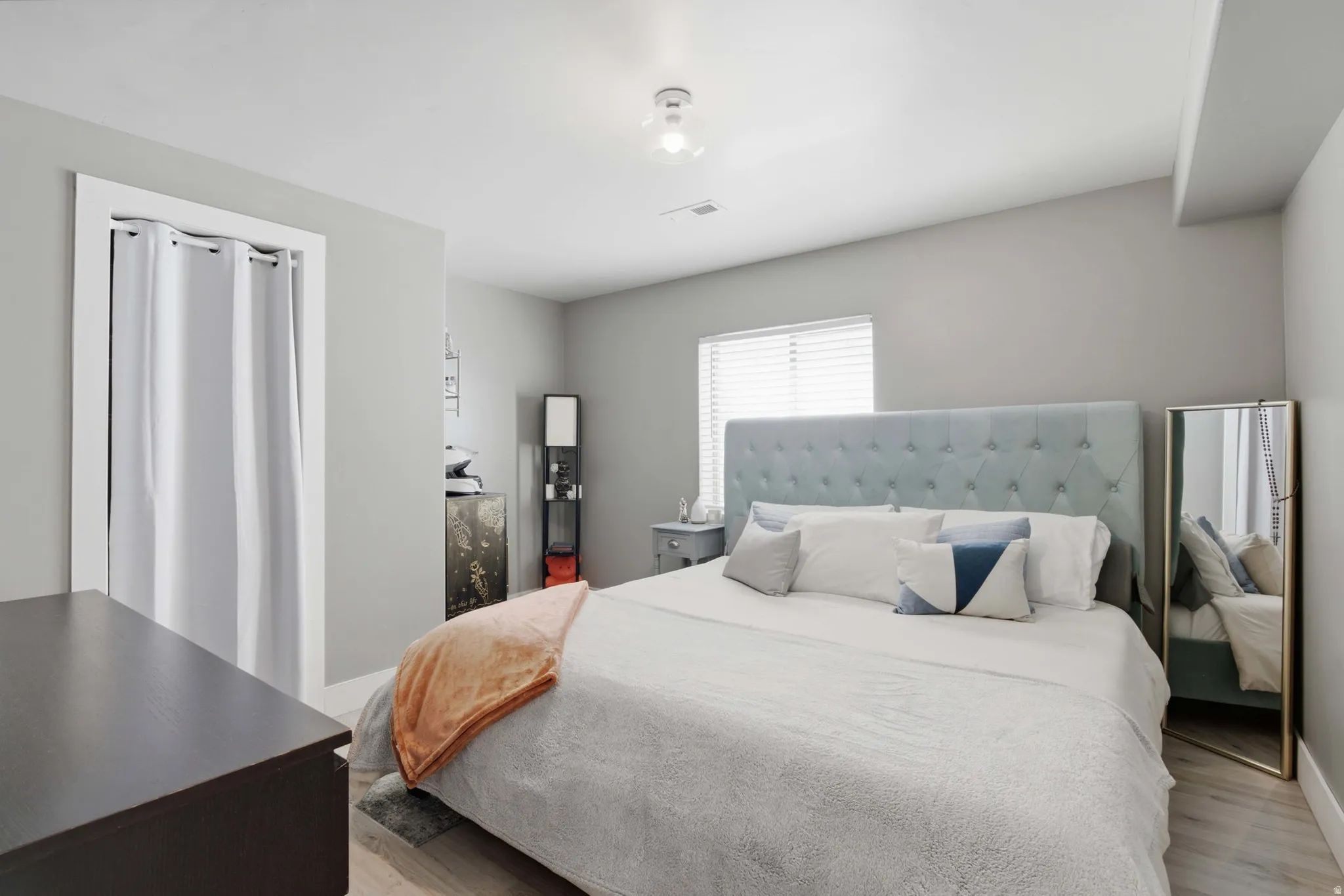 Spacious bedroom featuring a upholstered gray headboard, wood-finish flooring, and abundant natural light from a large window