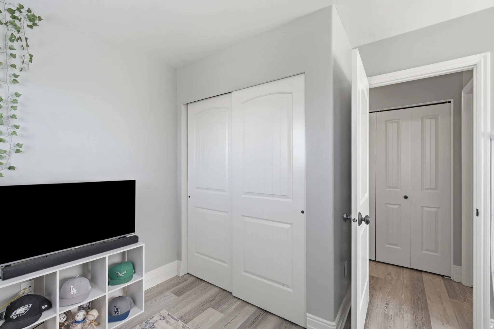 Light gray wall paint, wood-finish flooring, white bi-fold closet doors, white wall trim, and a paneled interior door