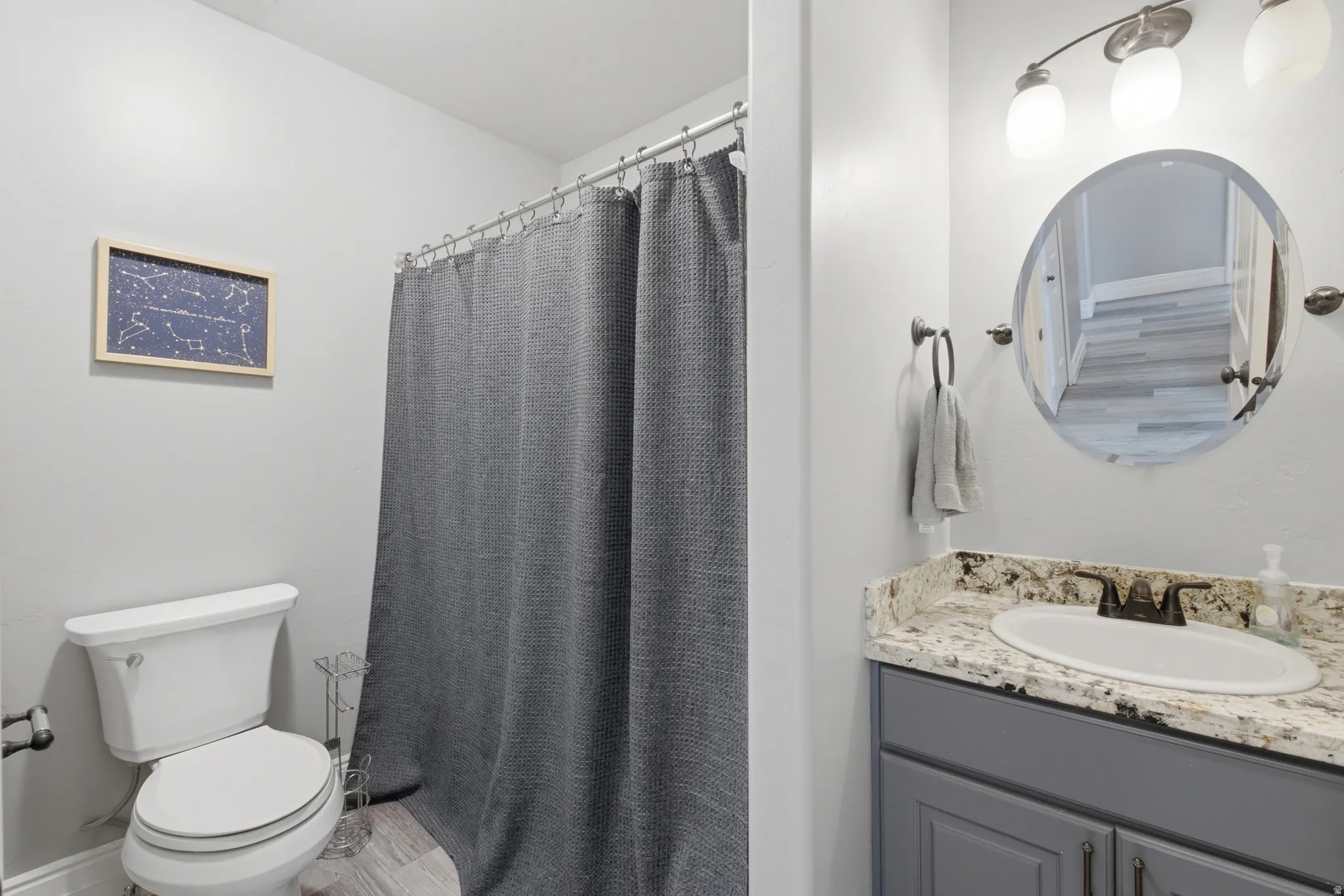 Bathroom featuring a vanity with a light-colored countertop, an undermount sink, a circular mirror, and a three-light fixture