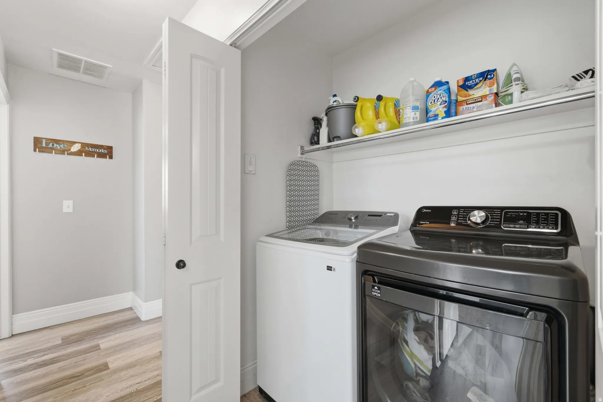 Dedicated laundry area featuring a built-in shelf, light-toned walls, and wood-finish flooring