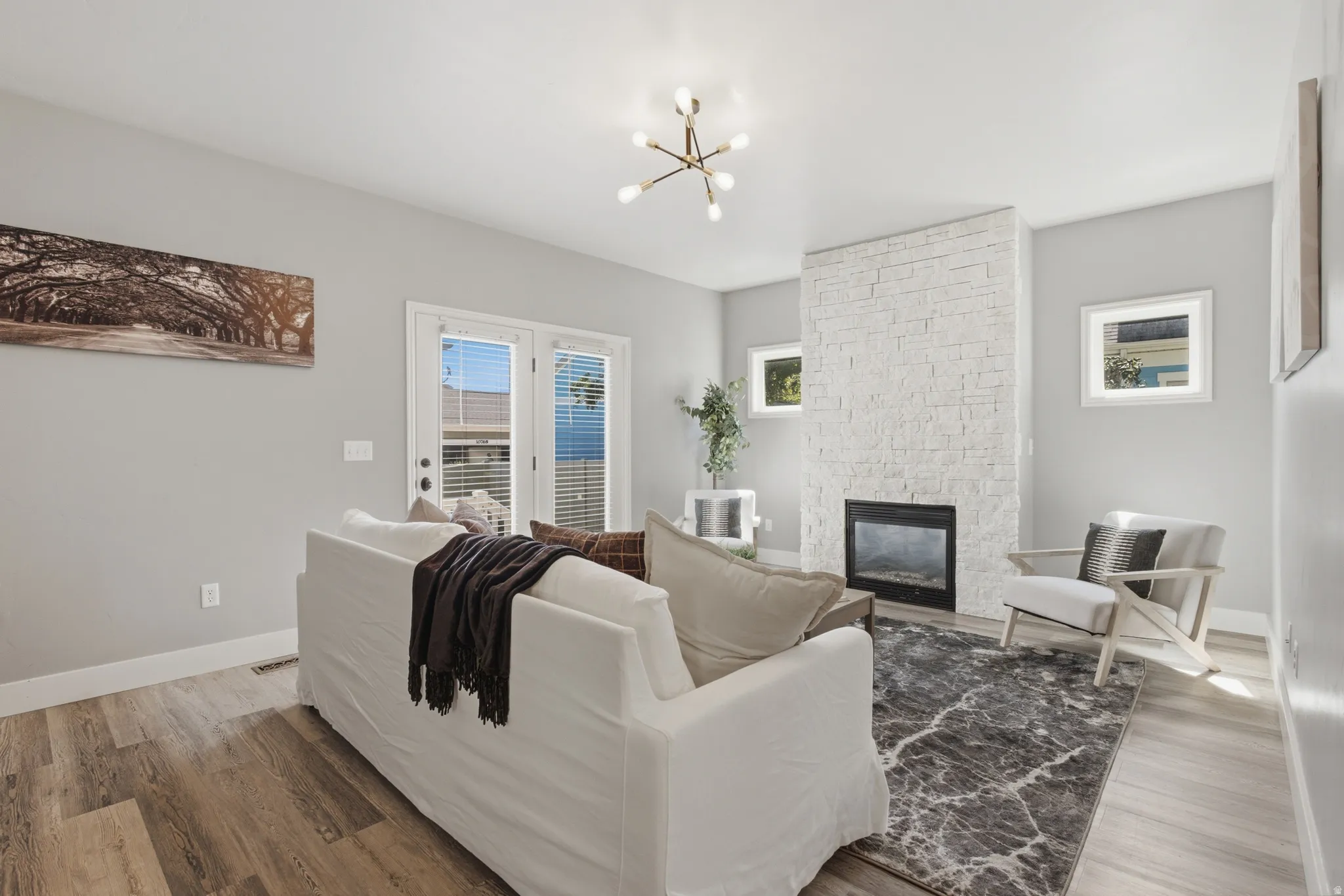 Second living area featuring wood-finish flooring, a white brick-finish fireplace, and double French doors with interior blinds