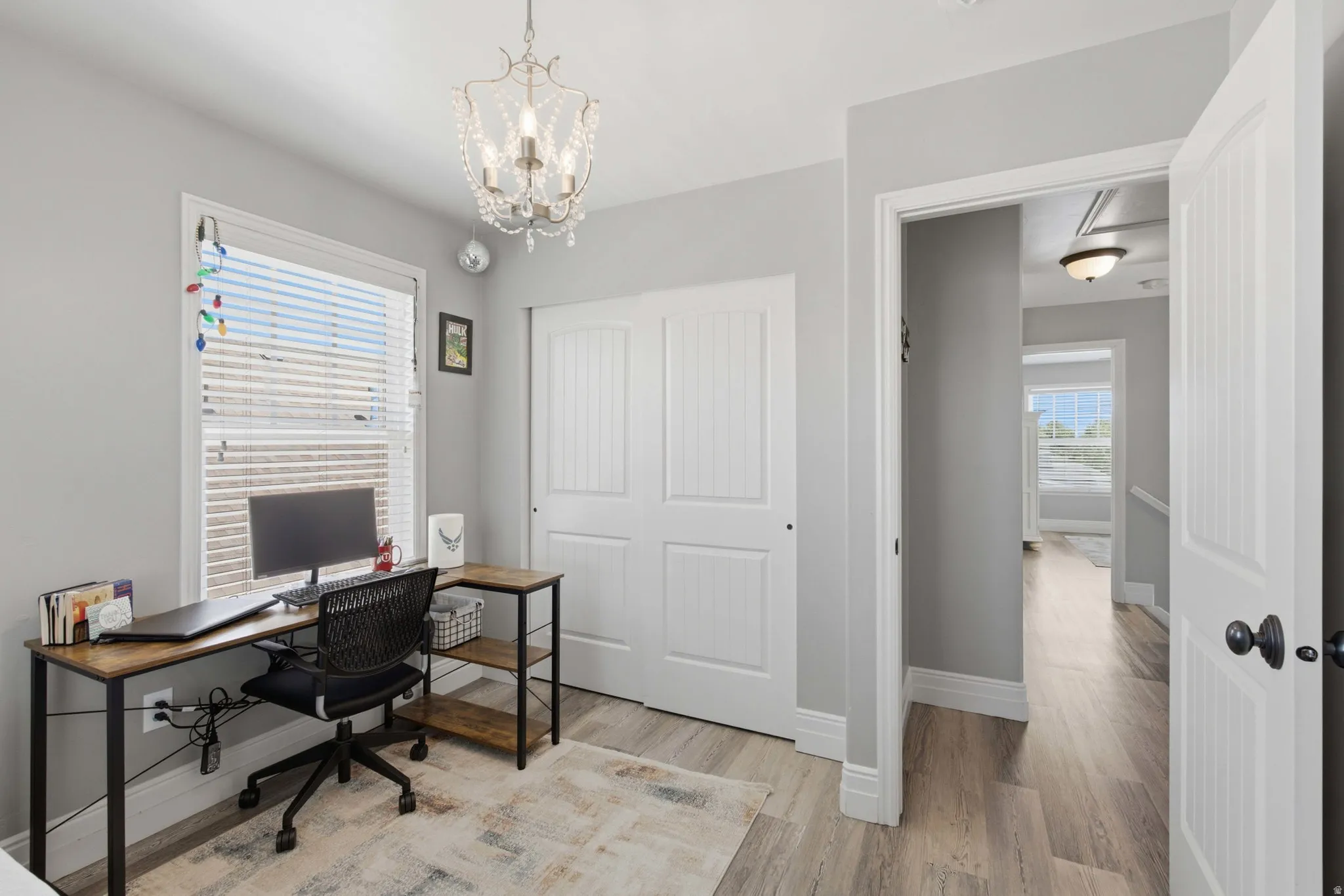 Recessed window with horizontal blinds, wood-finish flooring, white paneled bi-fold closet doors, and a decorative chandelier