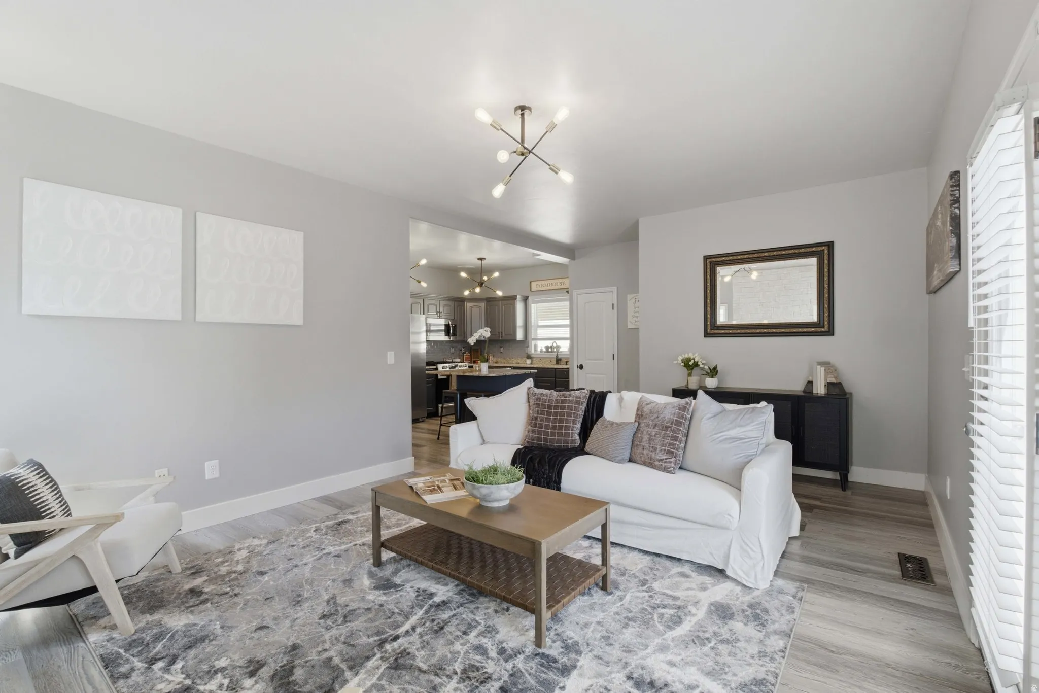 Open-concept living area with light gray walls, wood-finish flooring, and a contemporary ceiling fixture