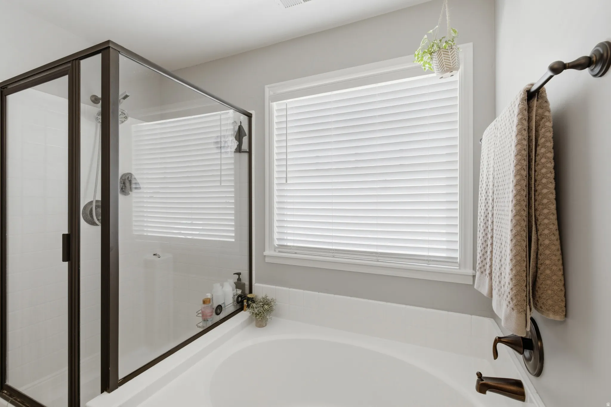 Owners ensuite, soaking tub with bronze-finish fixtures, glass-enclosed shower with tile surround, and a window with privacy blinds