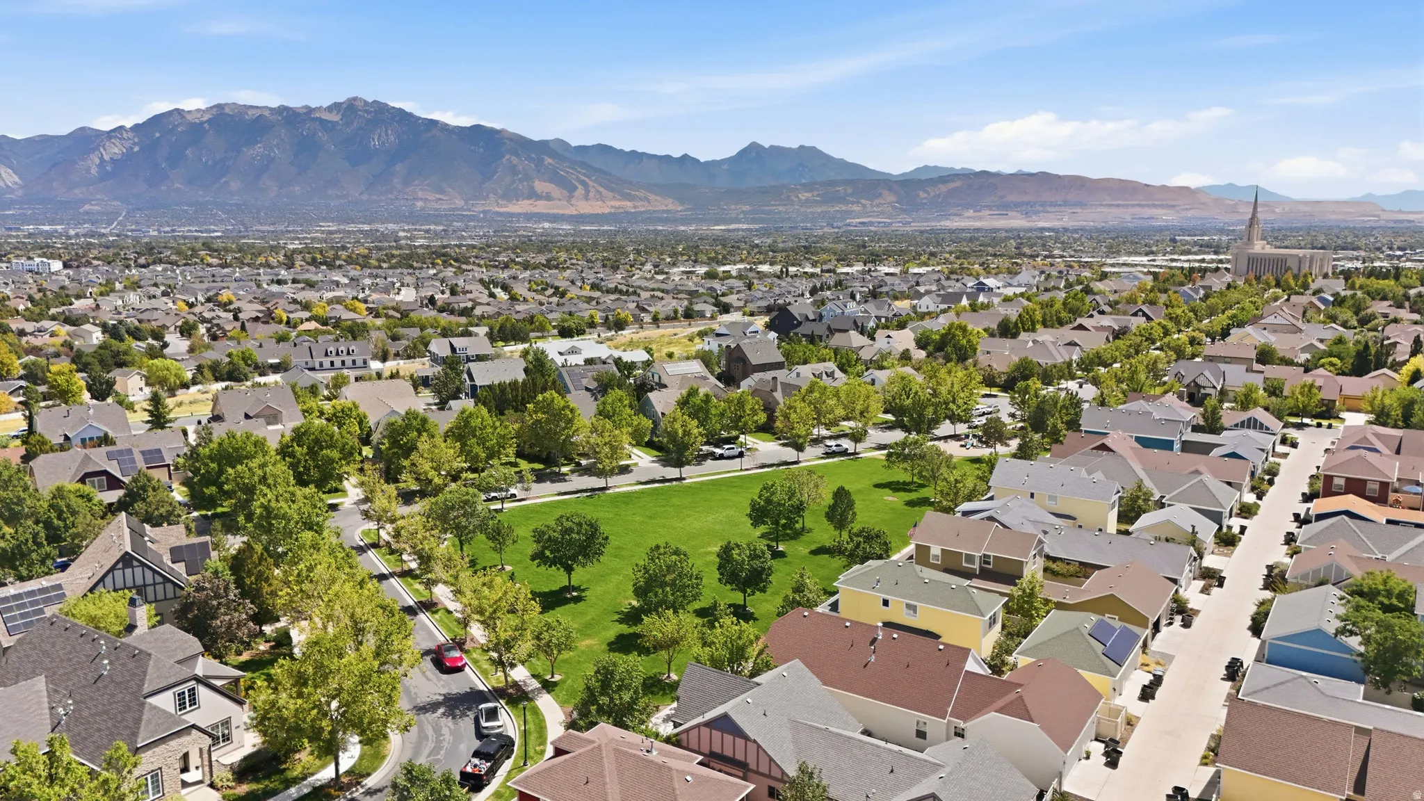 Expansive mountain backdrop, established neighborhood with mature trees, green space, and a visible religious edifice