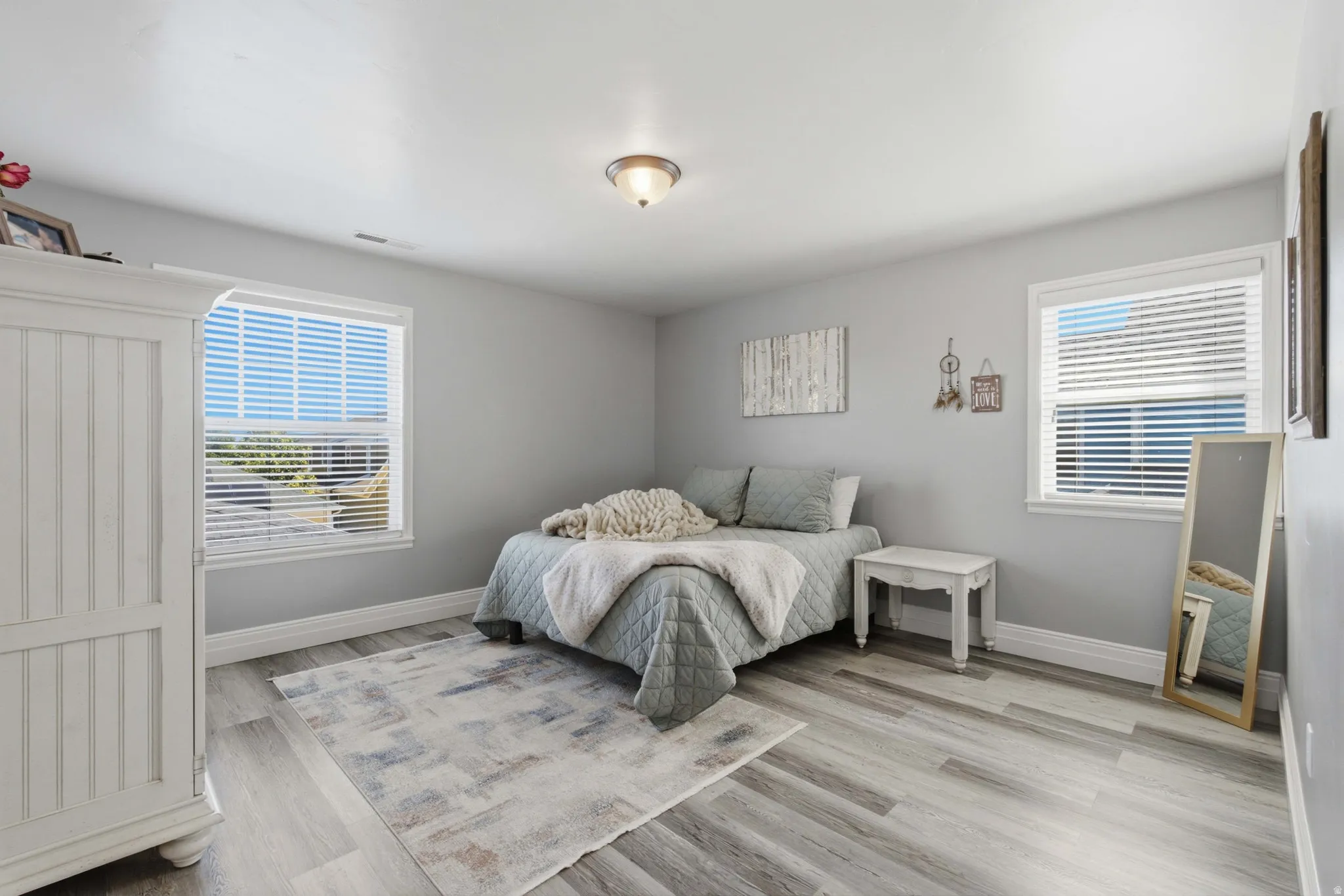 Owners suite, bright bedroom showcasing wood-finish flooring, dual windows with plantation shutters providing natural light, and a spacious layout
