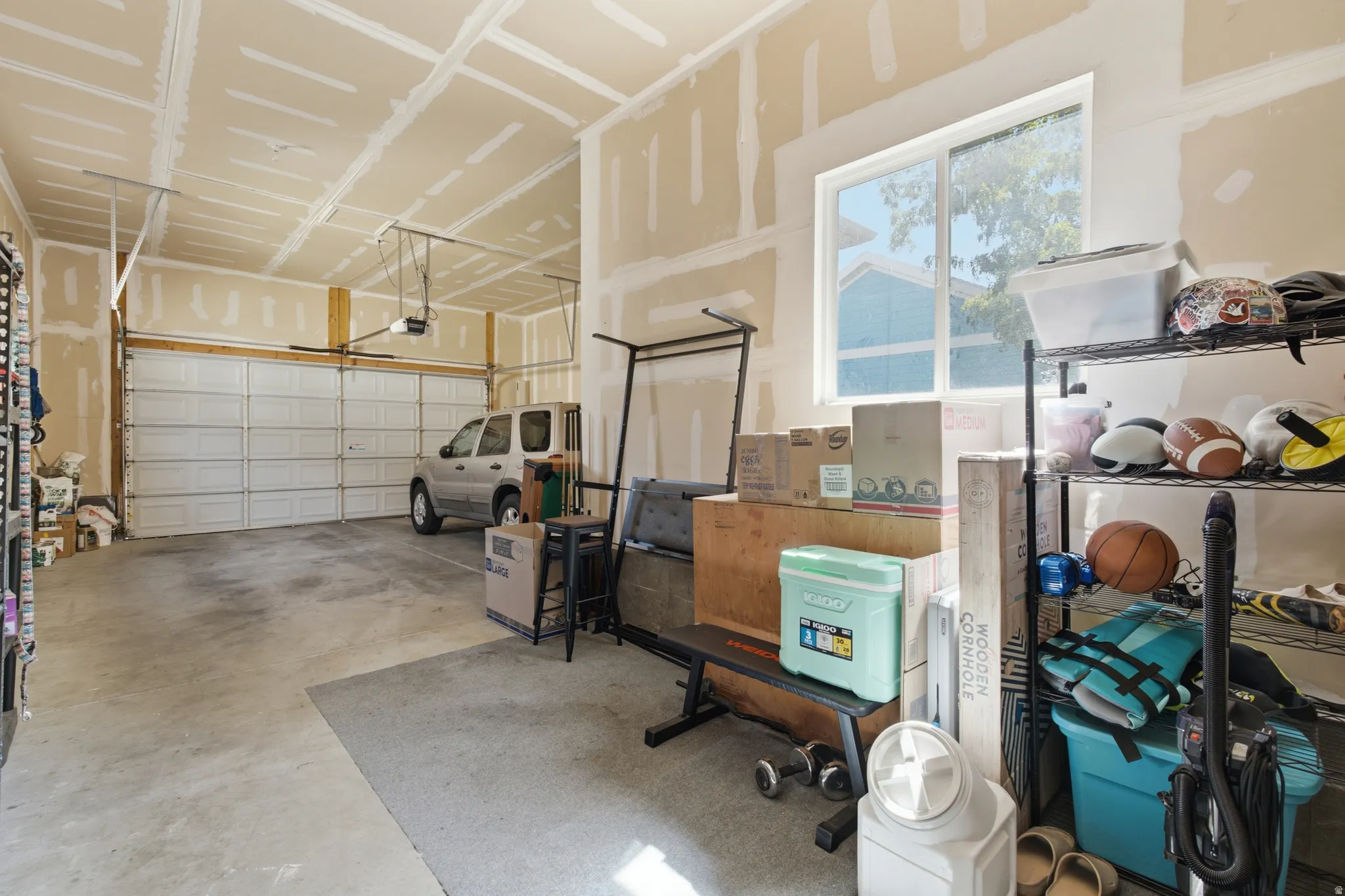 Attached three-car garage with concrete flooring, overhead garage door mechanisms, and a large window providing natural light. Ceilings are extra tall for future storage, very spacious.