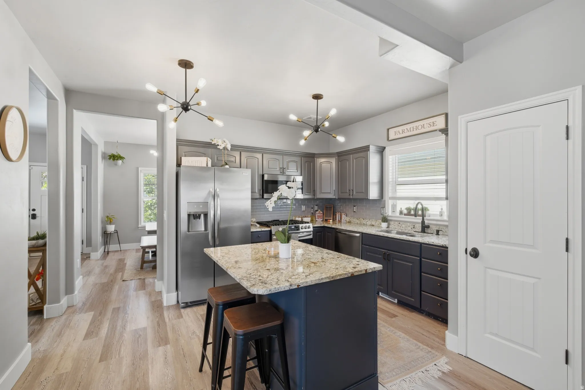 Kitchen featuring an island with stone countertop, stainless steel appliances, pendant lighting, shaker-style cabinetry, and wood-finish flooring