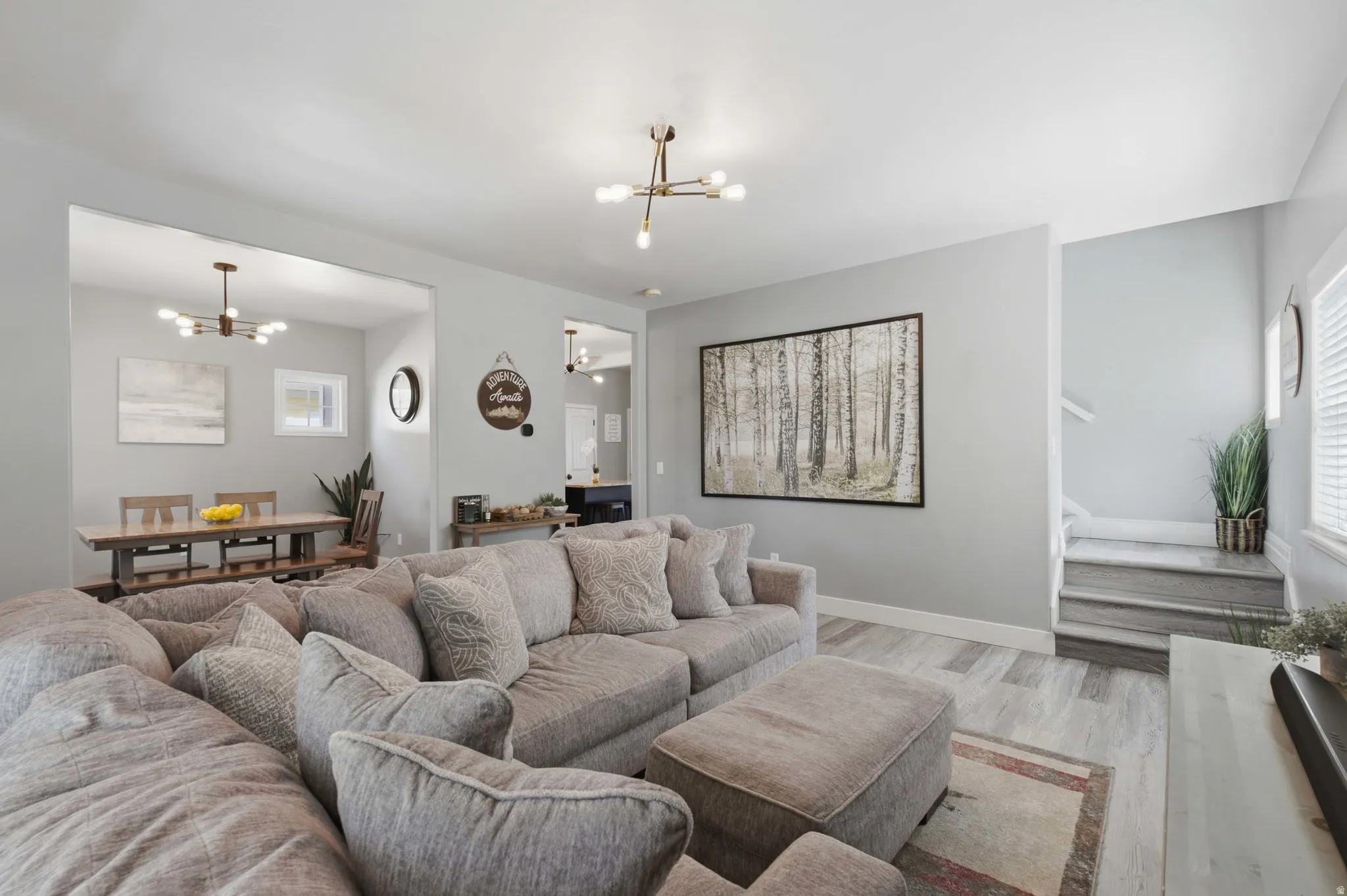 Expansive living area with wood-finish flooring, a modern chandelier, and a staircase featuring wood-finish treads
