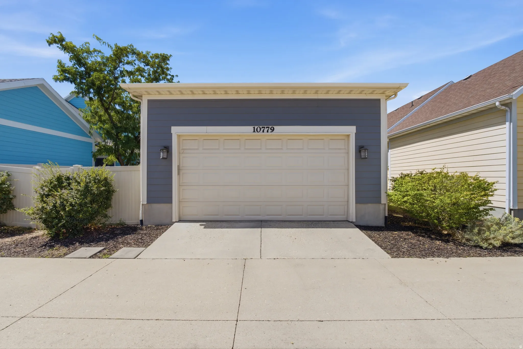Detached garage featuring a paneled door, gray siding, and exterior sconce lighting
