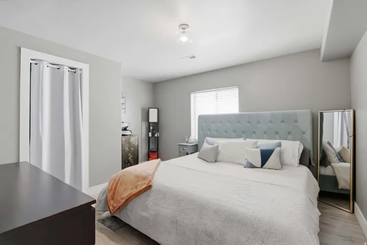 Spacious bedroom featuring a upholstered gray headboard, wood-finish flooring, and abundant natural light from a large window