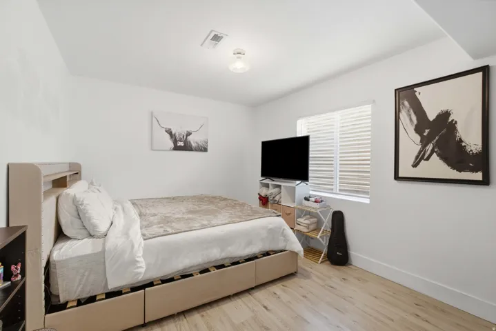 Light wood-finish flooring, white walls, and a single window with horizontal blinds