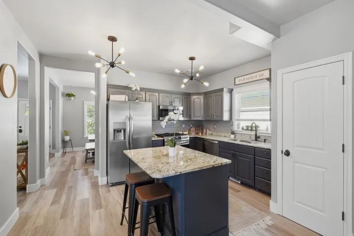 Kitchen featuring an island with stone countertop, stainless steel appliances, pendant lighting, shaker-style cabinetry, and wood-finish flooring
