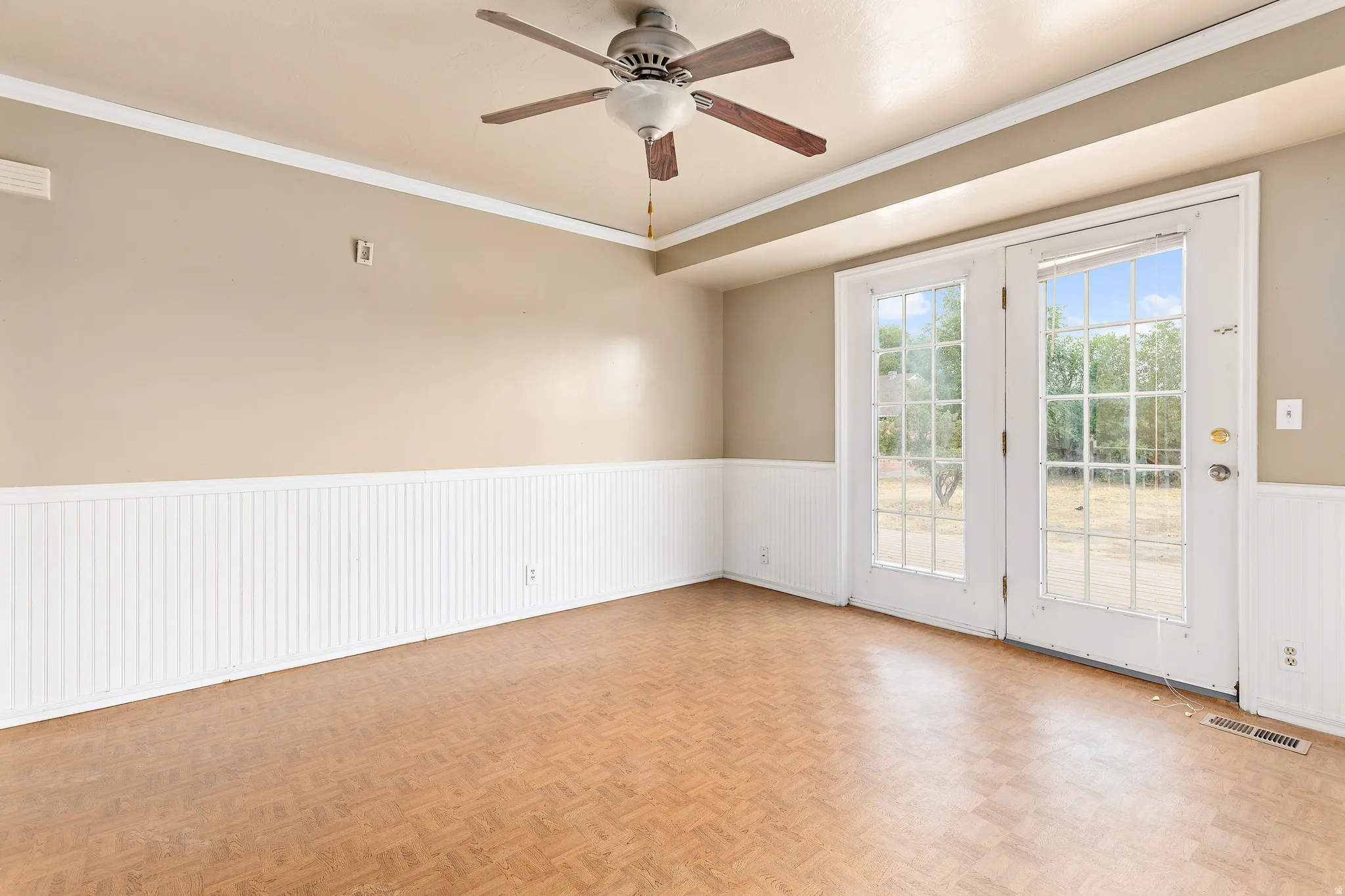 Ceiling fan with wood-finish blades, crown molding, beadboard wainscoting, and double French doors