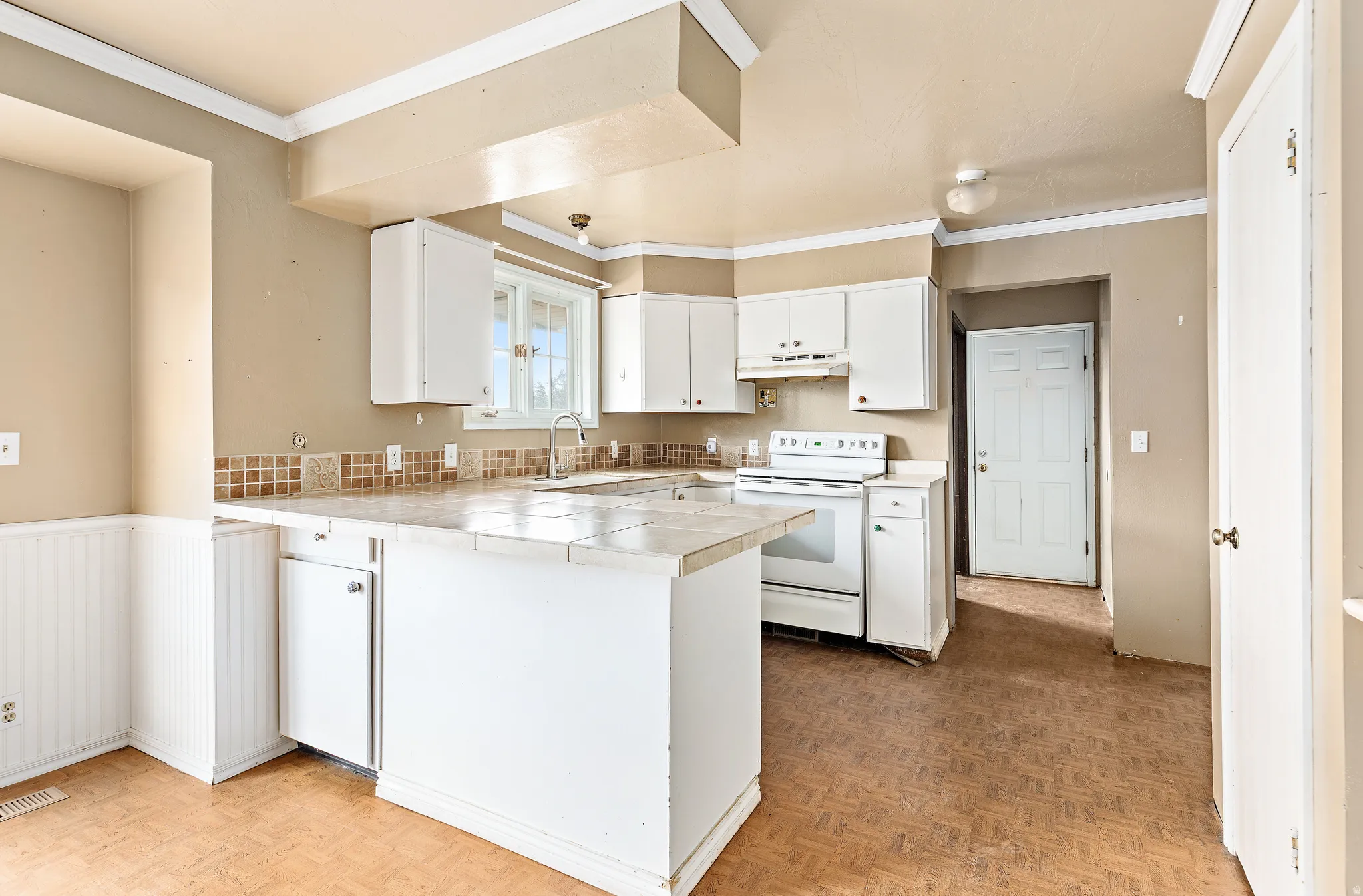 Kitchen featuring white cabinetry, tile countertops, a tile backsplash, and a window above the sink