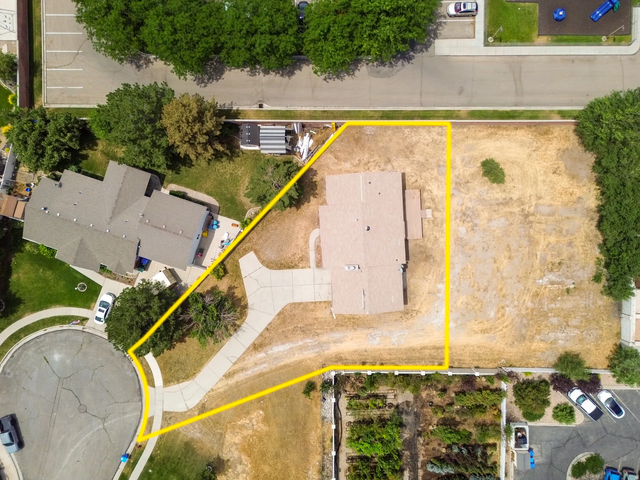 Expansive lot featuring a single-family residence with a multi-level roofline, extensive paved driveways, and surrounding undeveloped land