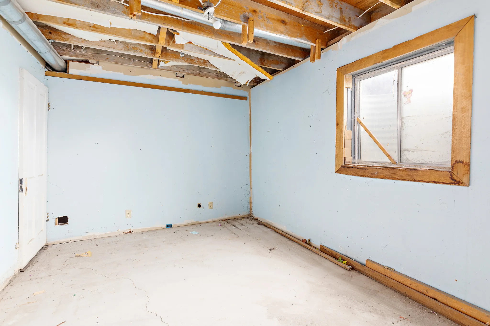 Concrete flooring, exposed ceiling joists, light blue wall finishes, and a wood-trimmed window