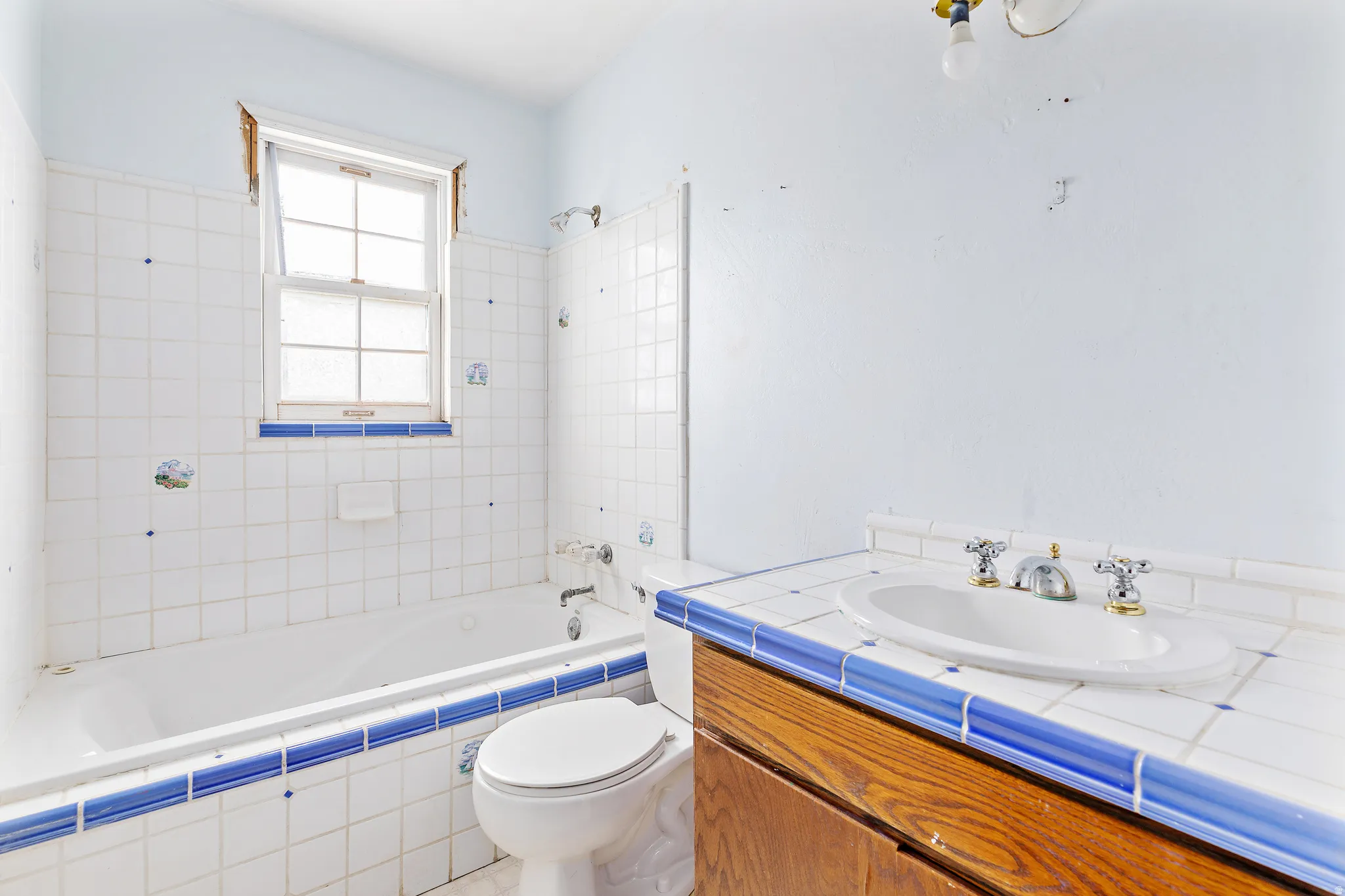 Bathroom featuring a window, tiled bath surround, built-in bathtub, toilet, and a vanity with an integrated sink
