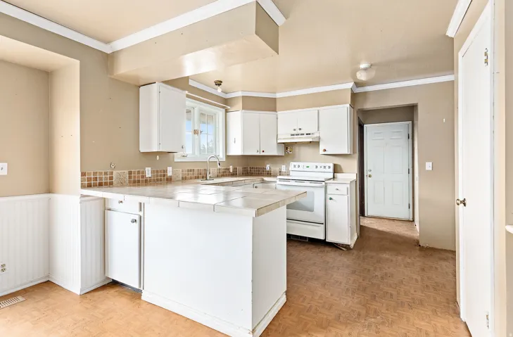 Kitchen featuring white cabinetry, tile countertops, a tile backsplash, and a window above the sink