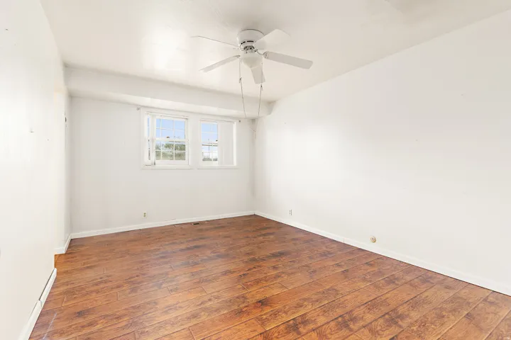 Wood-finish flooring, white walls, and a ceiling fan with integrated lighting