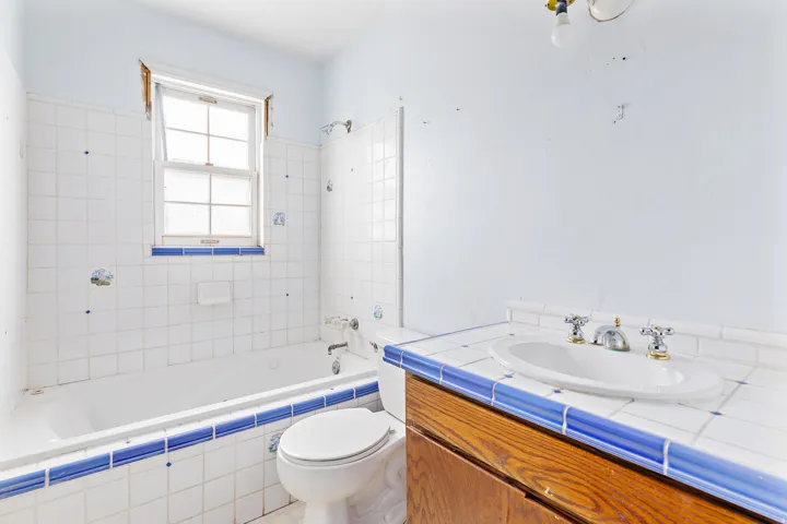 Bathroom featuring a window, tiled bath surround, built-in bathtub, toilet, and a vanity with an integrated sink