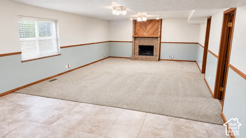 Spacious room featuring a brick fireplace, wood mantel with chevron detailing, light carpet, and tile flooring
