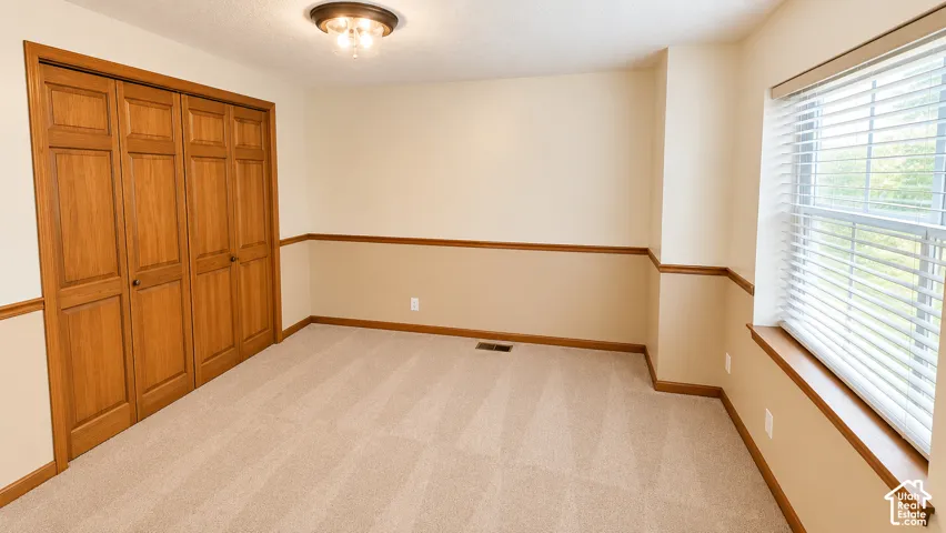 Light-colored wall-to-wall carpeting, wood-finish bi-fold closet doors, and a window with horizontal blinds