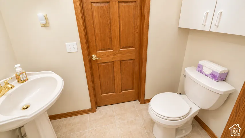 Pedestal sink with gold-finish faucet, white toilet, light wood-finish door, and integrated wall-mounted cabinetry