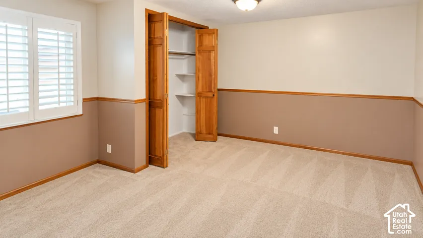 Carpeted flooring, bi-fold closet doors, built-in closet shelving, window with plantation shutters, and a flush-mount ceiling light fixture
