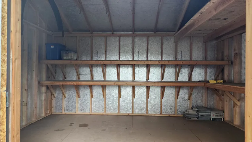 Interior storage structure with exposed wood framing, two built-in shelving units, a built-in corner workbench, and a corrugated metal interior wall finish