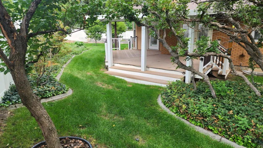 Expansive backyard featuring a manicured lawn, established perimeter landscaping, and a multi-level deck with white railings