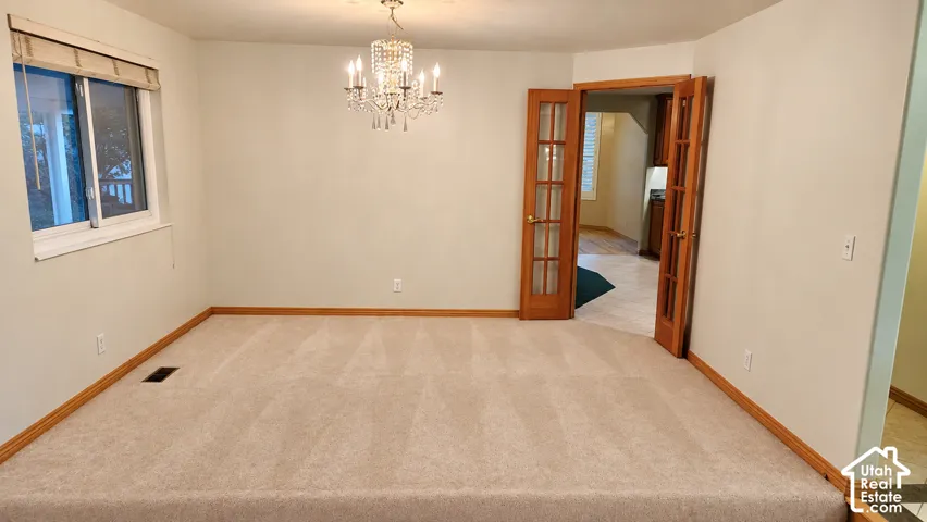 Carpeted room with a crystal chandelier and warm wood-framed French doors