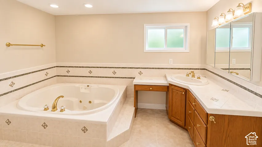 Recessed lighting illuminates a jetted tub set in tiled surround, complemented by a wood-finish vanity with an integrated sink, and an extended countertop
